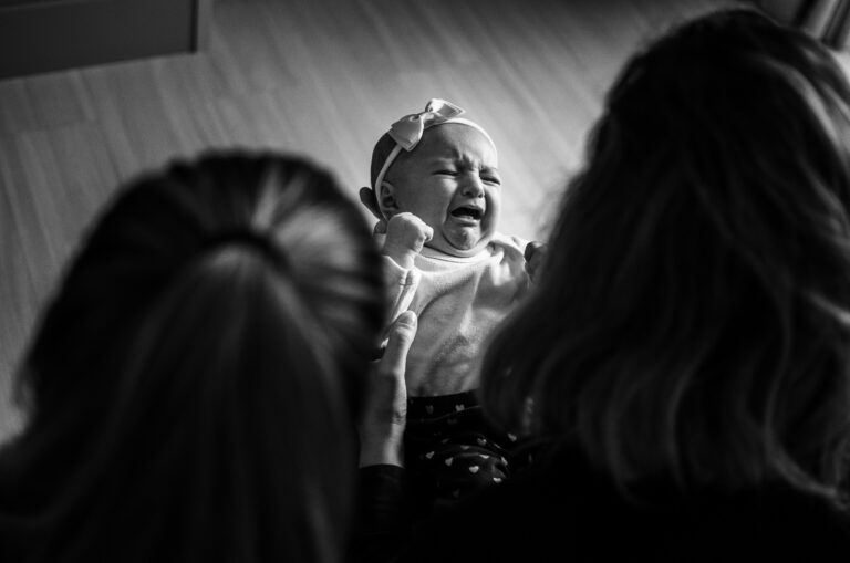 Bébé malade pleurant dans les bras de ses parents, montrant une détresse visible.